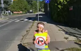 dziewczynka stoi pod znakiem drogowym zakaz skrętu w lewo trzyma w rękach obrazek tego znaku