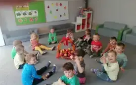 dzieci siedzą w kole na dywanie w środku stoi koszyk z jabłkami