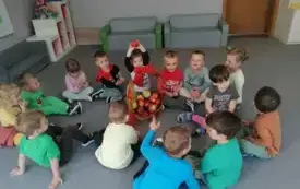 dzieci siedzą w kole na dywanie w środku stoi koszyk z jabłkami