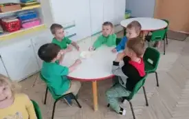 chłopcy siedzą przy okrągłym stole i jedzą pokrojone jabłka z talerzyka