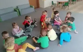 dzieci siedzą na dywanie pomiędzy nimi stoi koszyk z jabłkami