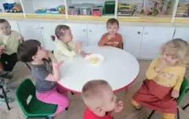 dzieci siedzą przy okrągłym stoliku i jedzą pokrojone jabłka z tależyka