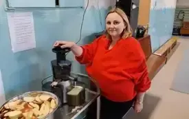 pani w przebraniu jabłka w czerwonej bluzie z opaska z liściem stoi przy sokowir&oacute;wce przed nią miska z pokrojonymi jabłkami
