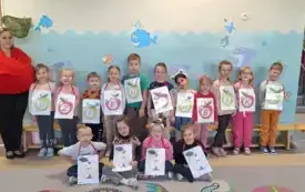 dzieci wraz z panią pozują do zdjęcia grupowego dzieci trzymają litery na szablonach jabłek tworzące napis dzień jabłka pani w czerwonej bluzie z opaską z listkiem 