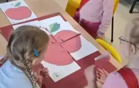 dziewczynki przy stole układają z element&oacute;w czerwone jabłko
