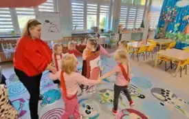 pani w czerwonej bluzie i opasce z zielonym listkiem stoi w kole z dziećmi w środku stoi dziewczynka z plakatem czerwonego jabłka