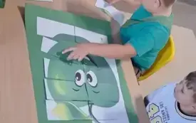 dw&oacute;ch chłopc&oacute;w przy stoliku układa z element&oacute;w plakat zielonego jabłka
