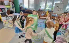 grupa dzieci w małym kole w środku stoi chłopiec z plakatem zielonego jabłka