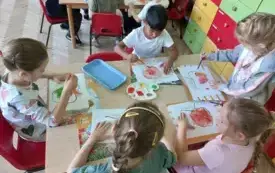 dzieci siedzą przy stoliku na kt&oacute;rym leżą farby dzieci malują folię bąbelkową na r&oacute;żne kolory pod folią leżą szablony jabłek