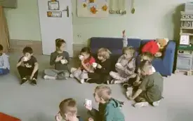 dzieci siedzą na dywanie i piją z kubeczk&oacute;w sok jabłkowy