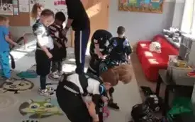 dzieci przebierające się w stroje hokejowe kt&oacute;re leżą na dywanie pośr&oacute;d dzieci stoi pan