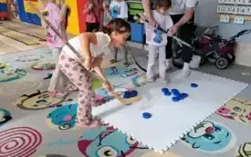 dziewczynki trzymające kije do gry w hokeja stoją przy białej macie na kt&oacute;rej leżą krążki do gry w hokeja pan pokazuje coś jednej z dziewczynek
