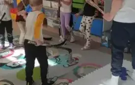 pan trzymający kij do hokeja stoi przed dziećmi na macie na kt&oacute;rej leżą niebieskie krążki hokejowe
