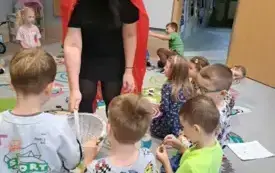 pani w stroju czerwonego kapturka rozdaje cukierki z koszyczka dzieciom siedzącym na dywanie
