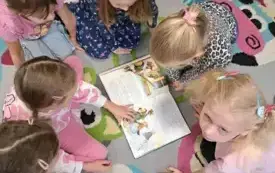 dziewczynki siedzą na dywanie dookoła rozłożonej książki 