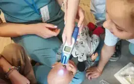 fantom noworodka na kolanach u pani pielęgniarki jedno z dzieci trzyma termometr elektroniczny przy czole noworodka