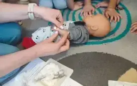 dzieci pochylone nad fantomem noworodka obok nich leżą akcesoria medyczne
