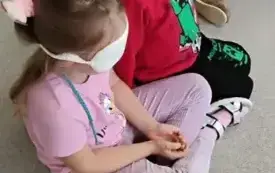 dziewczynka z zasłoniętymi oczami rozpoznaje co trzyma w dłoni w tle inne dzieci
