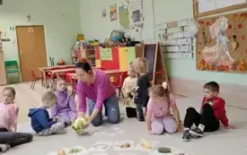dzieci siedzą w kole w środku leżą obrazki warzyw i owoc&oacute;w pani prezentuje dzieciom kalafiora