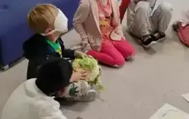 dzieci siedzą w kole chłopiec z zasłoniętymi oczami odgaduje co trzyma w dłoniach