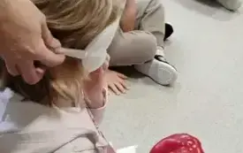dziewczynka z zasłoniętymi oczami rozpoznaje co trzyma w dłoni w tle inne dzieci