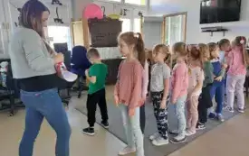 dzieci stoją w rzędzie przed panią kt&oacute;ra rozdaje im naklejki