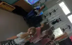 dzieci stoją na dywanie przed tablicą multimedialną na kt&oacute;rej widać obrazki przy tablicy stoi pani i m&oacute;wi do dzieci