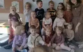 dzieci wraz z panią nauczycielką pozują do zdjęcia przed nimi stoi koszyk z kasztanami w tle dekoracja dzień kasztana