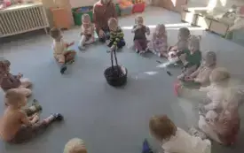 dzieci siedzą w kole na dywanie w środku stoi koszyk z kasztanami z dziećmi siedzi pani