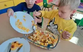 dw&oacute;ch chłopc&oacute;w przesypuje owoce z talerza do naczynia z owocami i galaretką 