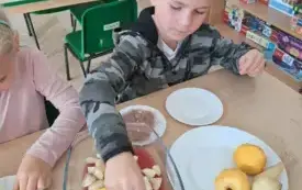 chłopiec wkłada pokrojone owoce do naczynia z galaretką na stole leżą obrane owoce i na talerzyku starta czekolada
