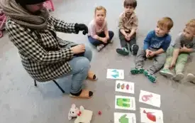 dzieci siedzą na dywanie przed nimi leżą na dywanie obrazki z elementami garderoby pani siedzi na krzesełku w ubraniu zimowym