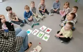 dzieci siedzą w p&oacute;łkolu przed nimi leżą na dywanie obrazki z elementami garderoby pani siedzi na krzesełku w ubraniu zimowym