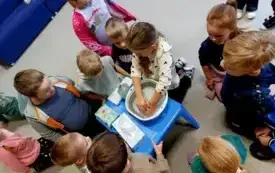 dziewczynka przy niebieskim stoliku myje ręce w misce z wodą i mydłem dookoła inne dzieci przyglądają się