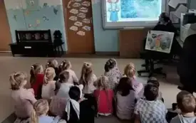 dzieci siedzą na dywanie i oglądają film edukacyjny na tablicy multimedialnej