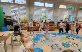 dzieci chodzą po niebieskich kołach wykonanych z folii z kolorowymi kijkami w rękach 