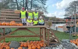 sześcioro dzieci w kamizelkach odblaskowych siedzi i stoi na ogromnej ławce obok leżą dynie dookoła widać dekoracje z dyniami