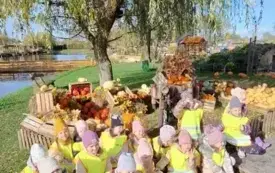 grupa dzieci w kamizelkach odblaskowych pozuje do zdjęcia na tle dekoracja z wielu dyń kwiat&oacute;w i innych element&oacute;w oraz wierzba płacząca