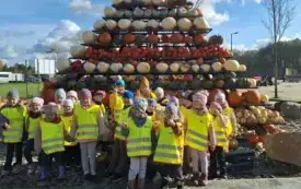 dzieci w kamizelkach odblaskowych pozują do zdjęcia grupowego w tle dekoracja z dyń w kształcie piramidy
