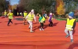 dzieci w odblaskowych kamizelkach skaczą na pomarańczowym dmuchańcu