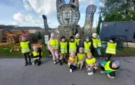 grupa dzieci w kamizelkach odblaskowych pozuje do zdjęcia na tle dekoracji w kształcie chińskiego kota z łapką w g&oacute;rze