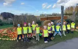 grupa dzieci w kamizelkach odblaskowych pozuje do zdjęcia na tle dekoracji w kształcie konia zaprzężonego do wozu wykonanej ze słomy