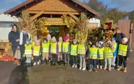 grupa dzieci wraz z trzema paniami pozuje do zdjęcia na tle domku z napisem dobronianka