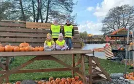 czworo dzieci w kamizelkach odblaskowych na ogromnej ławce obok leżą dynie dookoła widać dekoracje z dyniami