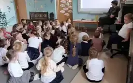 dzieci siedzą na dywanie przed nimi pan leśnik i tablica multimedialna na kt&oacute;rej odtwarzany jest film
