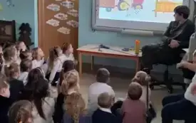 dzieci siedzą na dywanie przed nimi pan leśnik i tablica multimedialna na kt&oacute;rej odtwarzany jest film