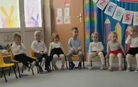 dzieci w odświętnych ubraniach siedzą na krzesełkach