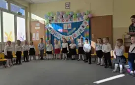 dzieci w odświętnych ubraniach stoją w p&oacute;łkolu za nimi dekoracja z napisem Pasowanie na przedszkolaka szablony kredek i balony
