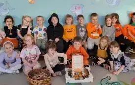 grupa dzieci wraz z panią pozuje do zdjęcia przed nimi stoi koszyk z cukierkami  pudełko z donatami i dyplom