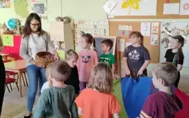 dzieci trzymają chustę klanzy przed nimi stoją dwie panie jedna trzyma kosz z cukierkami